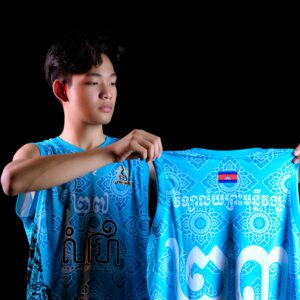 Young man displaying a vibrant sports jersey with intricate patterns and text on a black background in a studio setting.
